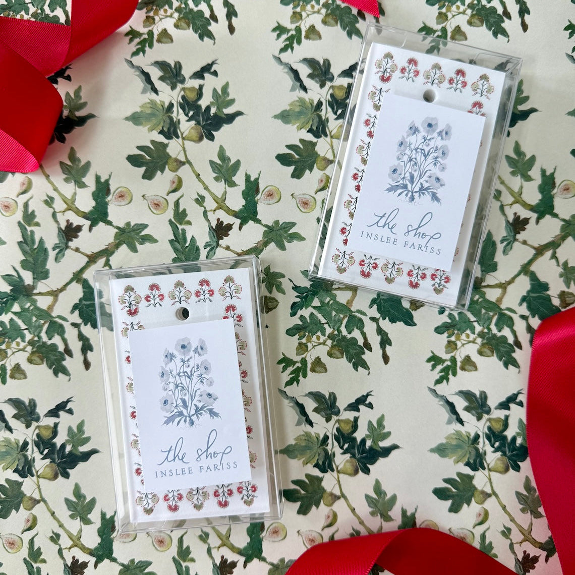 Two flat-printed gift tags with holiday motifs on a patterned background, one featuring a red ribbon bow and the other a white ribbon bow,